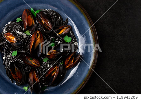 Spaghetti with black squid, black pasta, with boiled mussels, on a black plate, with parsley and parmesan cheese, close-up, selective focus, no people, Spaghetti with black squid, black pasta, with boiled mussels, on a black plate, with parsley and parmesan cheese, close-up, selective focus, no people, 119943209
