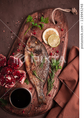 Fried dorado fish, with spices and herbs, on a wooden board, pomegranate sauce, close-up, no people, 119943248