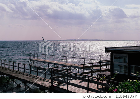 Seascape with sailing boat in the distance and pier Seascape with sailing boat in the distance and pier 119943357