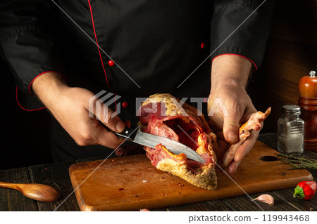 In the warm, cozy kitchen of the bar, an experienced chef confidently cuts duck meat, demonstrating culinary skills and the art of cooking In the warm, cozy kitchen of the bar, an experienced chef confidently cuts duck meat, demonstrating culinary skills and the art of cooking 119943468