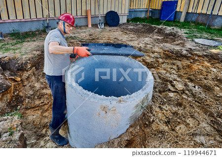 Builder installs support ring for manhole cover on concrete septic tank well. Builder installs support ring for manhole cover on concrete septic tank well. 119944671