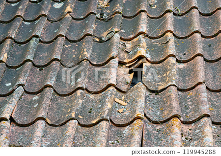 Damage to the clay tile roof of a historic house with some roof tiles missing, broken roof tiles 119945288