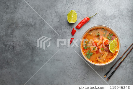 Spicy tom yum soup with shrimps, lime, chili pepper and coriander served in bowl top view, traditional Thai cuisine 119946248