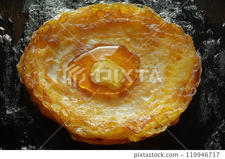 A close-up view captures a golden stack, emphasizing its crispy edges and fluffy center. Butter melts into the warm surface, while syrup pools invitingly, enhancing the dishs allure. 119946717