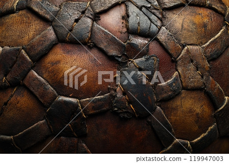 The image captures a close-up view of a worn soccer ball, showcasing its intricate leather patterns and stitching. The aged surface reflects years of use in vibrant play. The image captures a close-up view of a worn soccer ball, showcasing its intricate leather patterns and stitching. The aged surface reflects years of use in vibrant play. 119947003