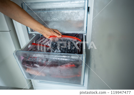 Girl hand taking frozen blueberry in bag from freezer. Stocking up for winter, diet Girl hand taking frozen blueberry in bag from freezer. Stocking up for winter, diet 119947477