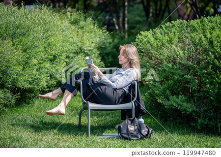 Relaxed self caring woman take break reading book comfortable sitting barefoot urban outdoor on lawn Relaxed self caring woman take break reading book comfortable sitting barefoot urban outdoor on lawn 119947480