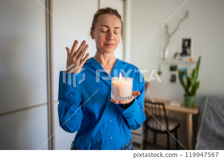 Aromatherapy at home. Balanced woman holding aesthetic burning aroma candle feeling warmth, pleasure 119947567