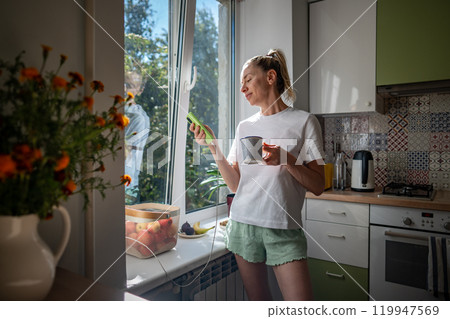 Lazy morning, procrastination with phone of woman drinking coffee in pajamas scrolling webs on phone 119947569