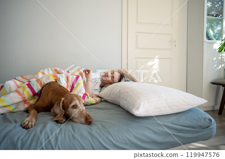 Lazy slow morning of awaked woman pet owner relaxed lying with vizsla dog in bed prepare starts day  119947576