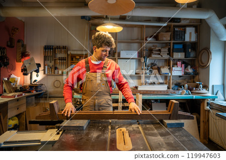 Content calm carpenter crafting wooden bed frame in workshop. Furniture from natural wood for sale 119947603