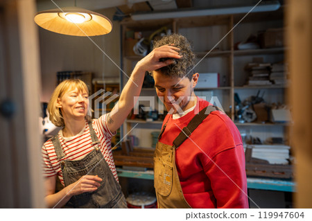 Laughing married couple of carpenters playfully joke around at work in woodworking shop. Teamwork Laughing married couple of carpenters playfully joke around at work in woodworking shop. Teamwork 119947604