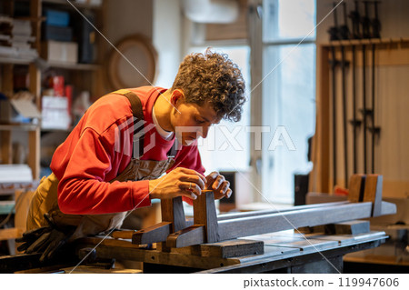 Focused woodworker applies leather pads to bed legs in workshop, enhancing stability and protection Focused woodworker applies leather pads to bed legs in workshop, enhancing stability and protection 119947606