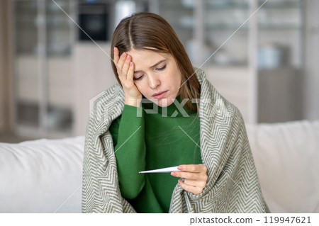 Sad sick woman measure temperature, holding head in hands on couch, suffer from headache and illness Sad sick woman measure temperature, holding head in hands on couch, suffer from headache and illness 119947621