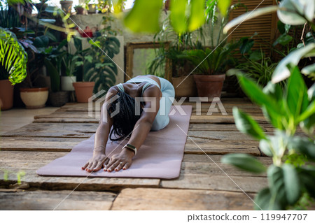 Sported black woman doing stretching exercise for back flexibility relaxation muscles on fitness mat 119947707