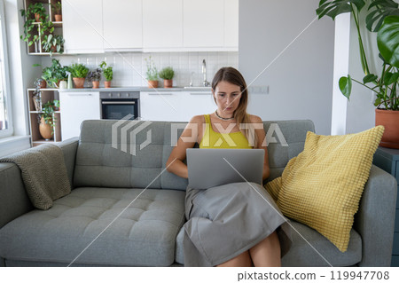 Serious focused woman uses laptop sit on sofa concentrating on remote work solving business issues. Serious focused woman uses laptop sit on sofa concentrating on remote work solving business issues. 119947708