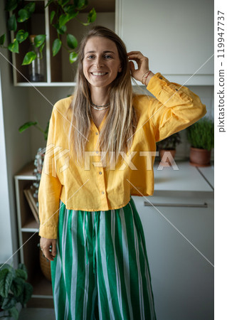 Portrait jolly happy female in yellow clothing looking at camera with cheerful smile, touching hair. 119947737