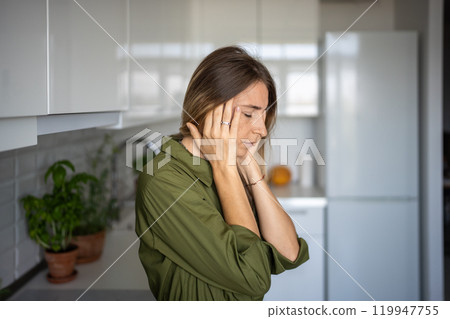 Tired woman feeling headache rubbing temples standing on kitchen with closed eyes. 119947755