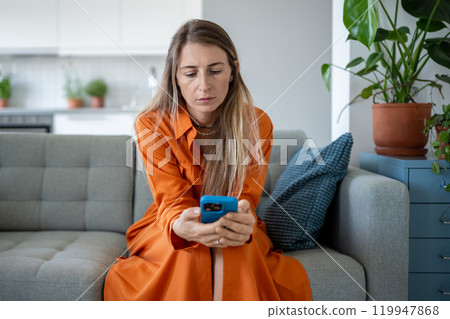 Stressed woman looks at smartphone screen, sad female reading unpleasant news on mobile phone. 119947868