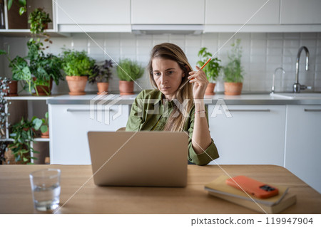 Busy thoughtful female sitting in kitchen, working freelance at home, reading attentively, thinking Busy thoughtful female sitting in kitchen, working freelance at home, reading attentively, thinking 119947904