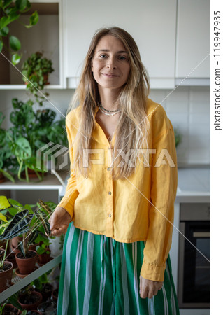 Cheerful woman gardener surrounded green indoor plants arranged by kitchen. Bright image plant lover 119947935
