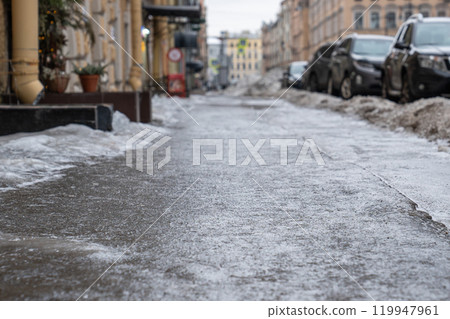 Slippery sidewalk in the city. Pavement covered with slippery ice. Frozen rain.  119947961