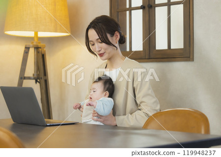 A woman in a suit holding a baby and working 119948237