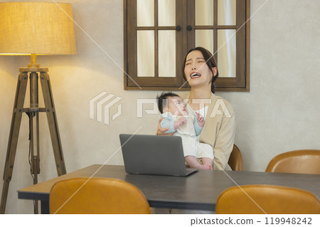 A woman in a suit holding a baby and working 119948242