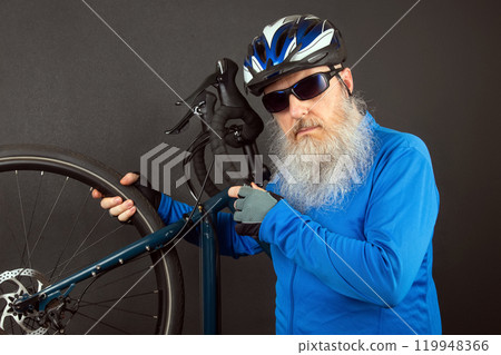 studio portrait of a cyclist in a helmet with a large white beard holding a bicycle in his hands studio portrait of a cyclist in a helmet with a large white beard holding a bicycle in his hands 119948366