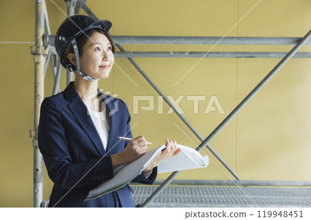 A woman in a suit looking at blueprints at the construction site 119948451