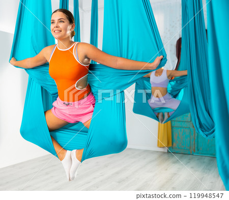 Girl performing butterfly pose holding hanging hammock with hands like wings 119948547