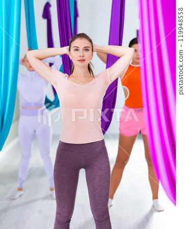 Fit young woman doing articular gymnastics with group in aerial yoga studio 119948558