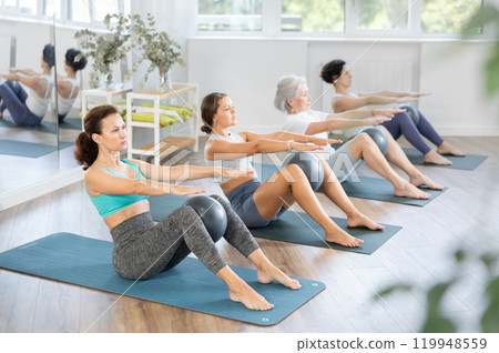 Woman performing set of exercises with pilates balls during group class with of different ages in fitness studio 119948559