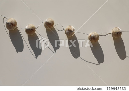 Elegant trendy paper christmas ornaments balls garland on beige table background in sunlight, long shadows. Minimal boho Scandinavian festive decoration. Handmade paper New Year party decor. 119948583