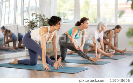 Latina stretching into Half Monkey Pose during group yoga practice Latina stretching into Half Monkey Pose during group yoga practice 119948606