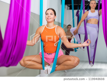 Girl sitting in butterfly pose in suspended hammock with fingers folded in mudra Girl sitting in butterfly pose in suspended hammock with fingers folded in mudra 119948608