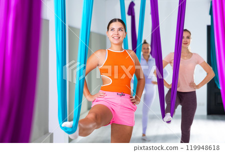 Young girl practicing group aerial yoga with hanging hammock 119948618