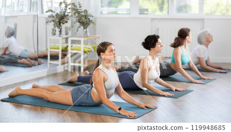 Group of women bending in back while lying on stomach in Bhujangasana Cobra Stretch position during training together in studio Group of women bending in back while lying on stomach in Bhujangasana Cobra Stretch position during training together in studio 119948685