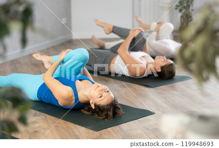 Woman doing Ardha Pawanmuktasana with group in yoga studio 119948693