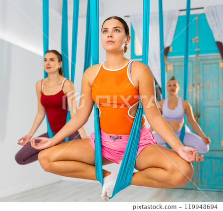 Girl doing bound angle pose in hanging hammock during aerial yoga Girl doing bound angle pose in hanging hammock during aerial yoga 119948694