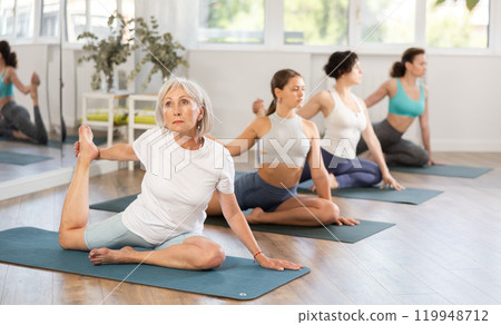 Elderly woman doing one legged king pigeon pose during yoga training Elderly woman doing one legged king pigeon pose during yoga training 119948712