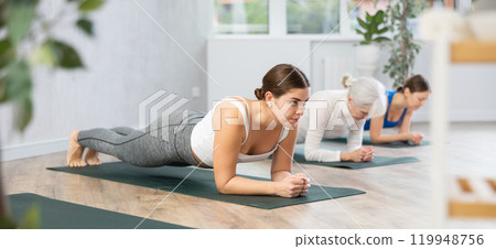 Young woman holding forearms plank pose in yoga studio Young woman holding forearms plank pose in yoga studio 119948756