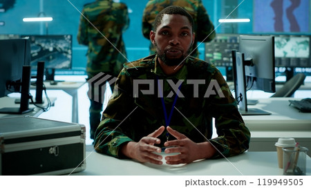 Military intelligence expert conducts a strategic teleconference connection in a modern command post, utilizing real time data on multiple screens for communication and decision making. Camera A. Military intelligence expert conducts a strategic teleconference connection in a modern command post, utilizing real time data on multiple screens for communication and decision making. Camera A. 119949505