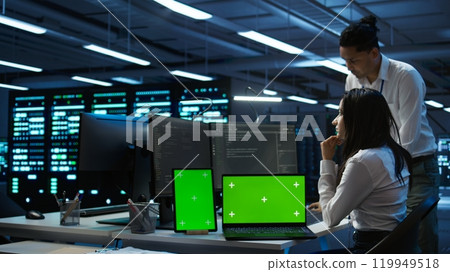 Engineers in data center monitoring security threats using chroma key devices. Experts using isolated screen tablet and laptop, ensuring compliance with regulations, camera B Engineers in data center monitoring security threats using chroma key devices. Experts using isolated screen tablet and laptop, ensuring compliance with regulations, camera B 119949518