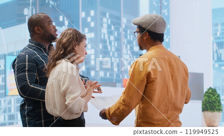 Corporate team reviewing architectural plans for a new office, discussing the building layout and the blueprints, potential investment opportunity in real estate during an office tour. Camera B. 119949525