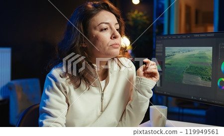 Video editor polishing raw footage, applying editing techniques, enhancing clarity, sharpness and brightness. Videographer adjusting clips while enjoying cup of coffee in office, camera B 119949561