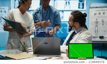 Licensed doctor and his staff review x ray scan results next to isolated copy space screen, examining hospital records before putting a diagnosis. Consulting analytics and radiography. Camera B. 119949578