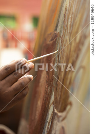 Focused man painting a new rustic artwork on canvas with brushstrokes patterns, mixing watercolors and applying to create a masterpiece. Young male artist working on his creation. Close up. Focused man painting a new rustic artwork on canvas with brushstrokes patterns, mixing watercolors and applying to create a masterpiece. Young male artist working on his creation. Close up. 119949646