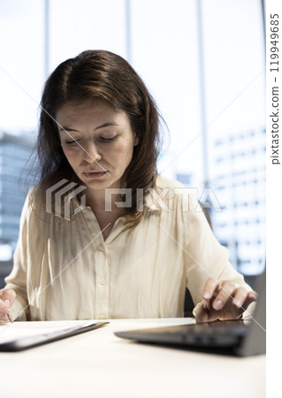Successful businesswoman manages a global enterprise and signing documents, reading legal paperwork to give her authorization. Highlighting her leadership qualities and expertise 119949685