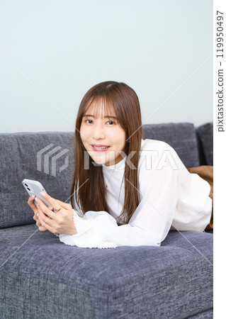 穿著休閒服的年輕女性躺在沙發、客廳、智慧型手機上 119950497